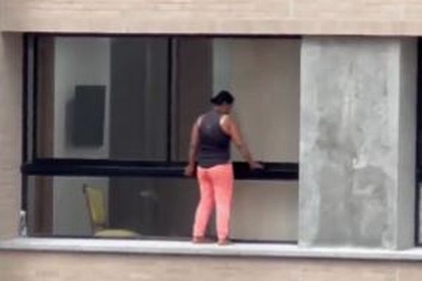 恐れ知らずの女性、安全具も身に着けず、高層マンションの縁で窓を拭く