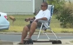 ハワイの歩道で、電動スケートボードにビーチチェアを付けて男性が走行